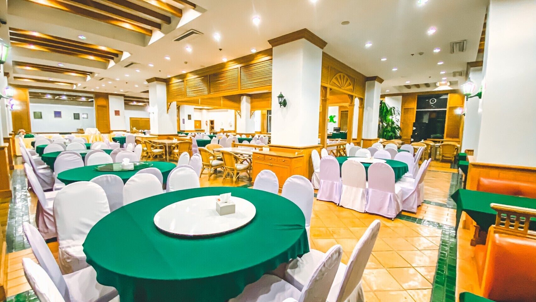 Une salle de banquet avec des tables rondes recouvertes de nappes vertes, des chaises blanches et un buffet central.