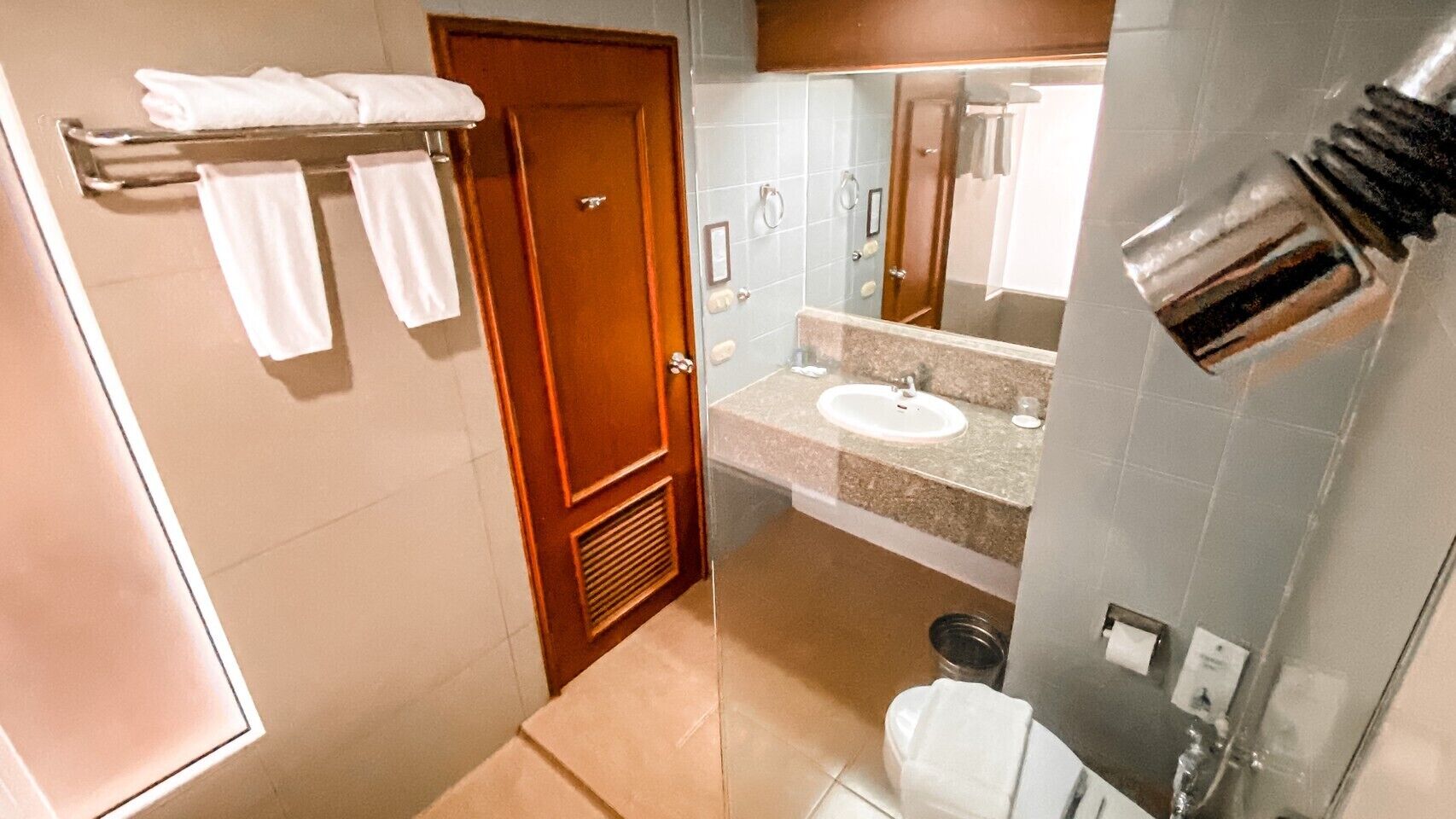 A bathroom with a wooden door, a sink, a mirror, and a towel rack.