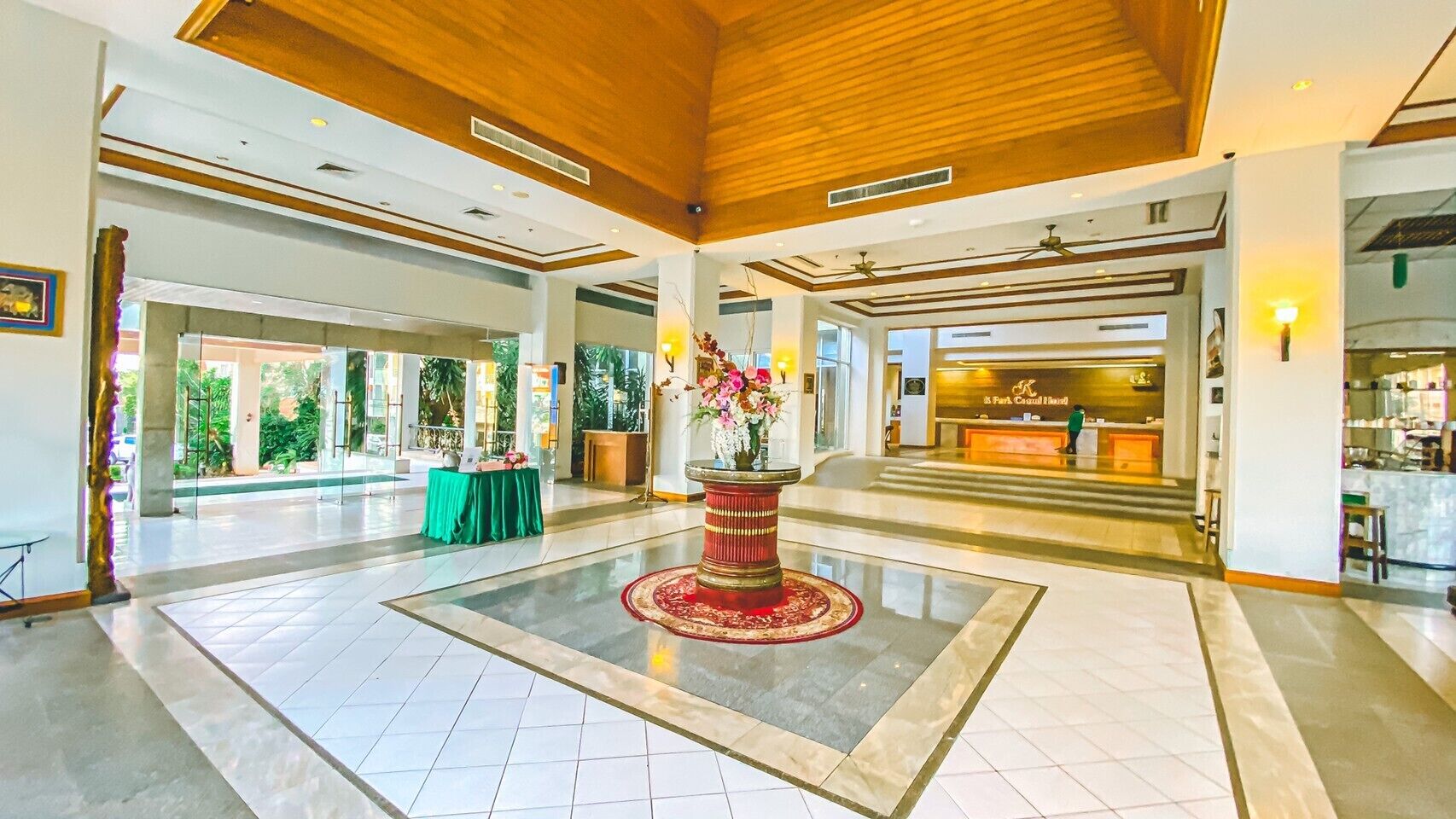 A spacious lobby with a central red and gold decorative piece, a reception desk, and a view of the outside through large windows.