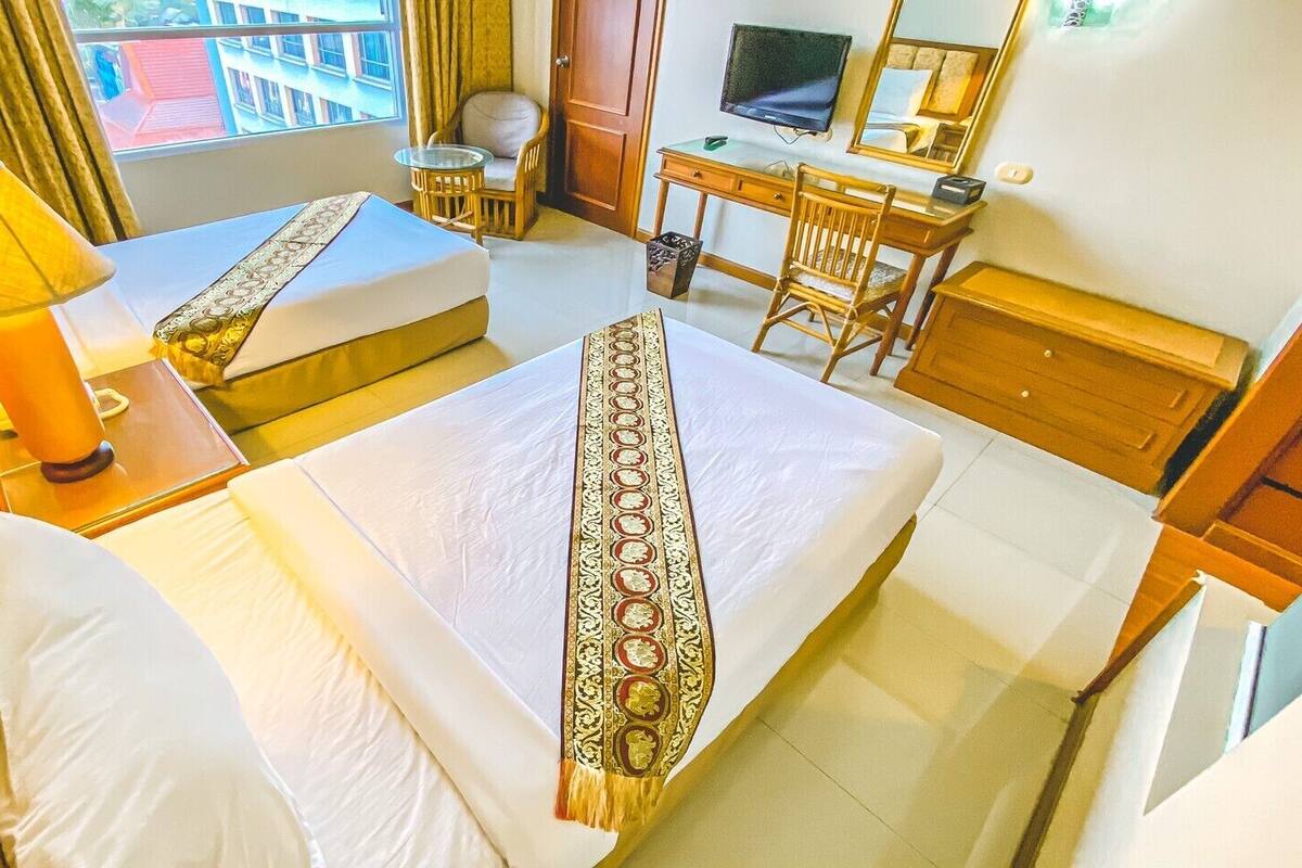 Une chambre d’hôtel avec deux lits, un bureau, une chaise, une télévision et une fenêtre avec des rideaux.