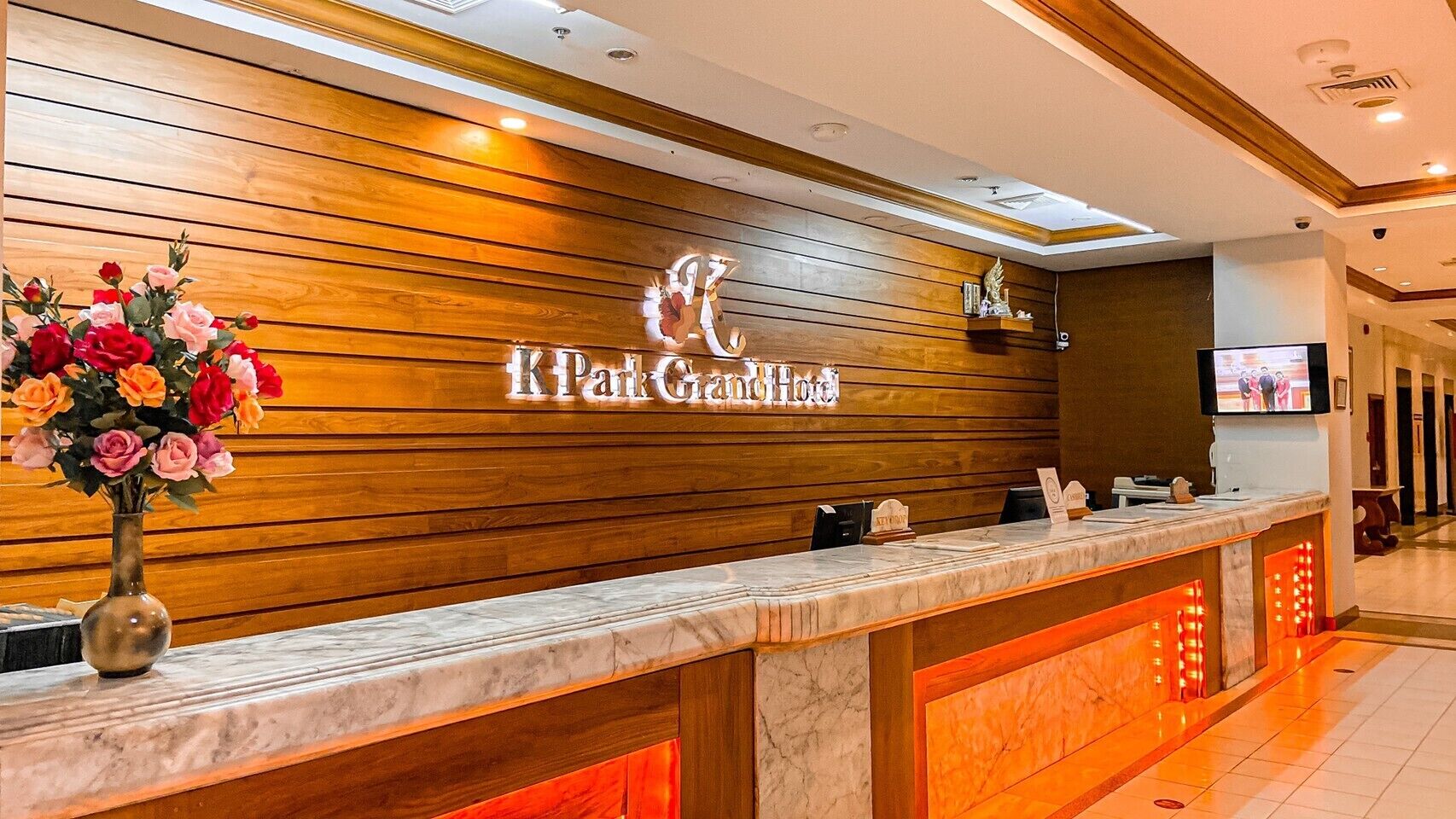A hotel reception desk with a wooden panel wall, a marble counter, and a vase of flowers.