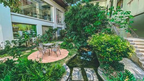 A courtyard with a small pond, surrounded by lush greenery and a seating area with chairs and a table. - K Park Grand Hotel (Surat Thani)