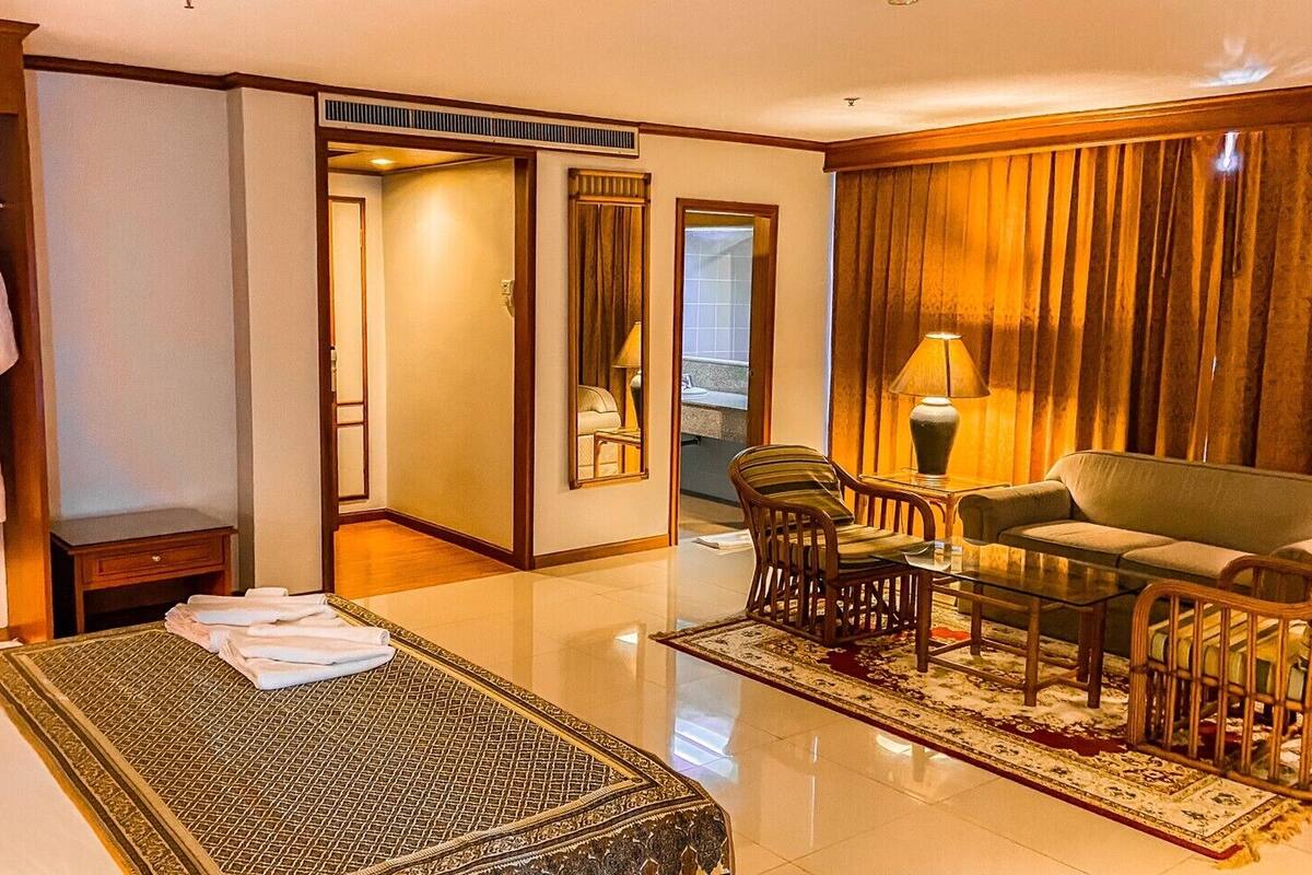 Une chambre d’hôtel comprenant un lit, un coin salon avec un canapé et des fauteuils, un miroir, une armoire et une salle de bain visible à travers une porte ouverte.