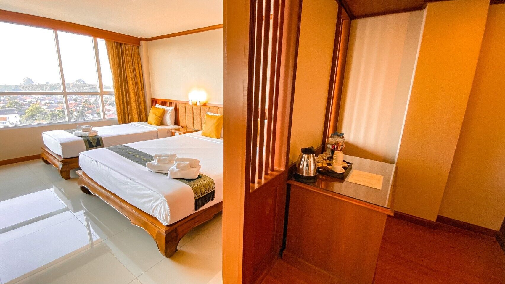 A hotel room with two beds, a small sitting area, a window with curtains, and a view of the city.
