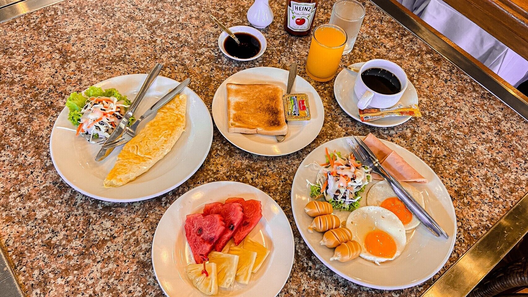 A breakfast buffet with plates of food, condiments, and beverages on a granite countertop.