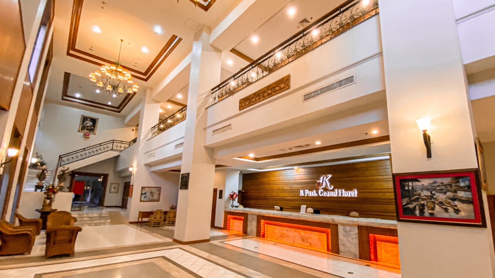 A grand hotel lobby with a reception desk, multiple seating areas, and a staircase.