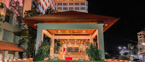 Entrada de hotel con un área techada, escalones que conducen a la entrada y un camino bien iluminado.