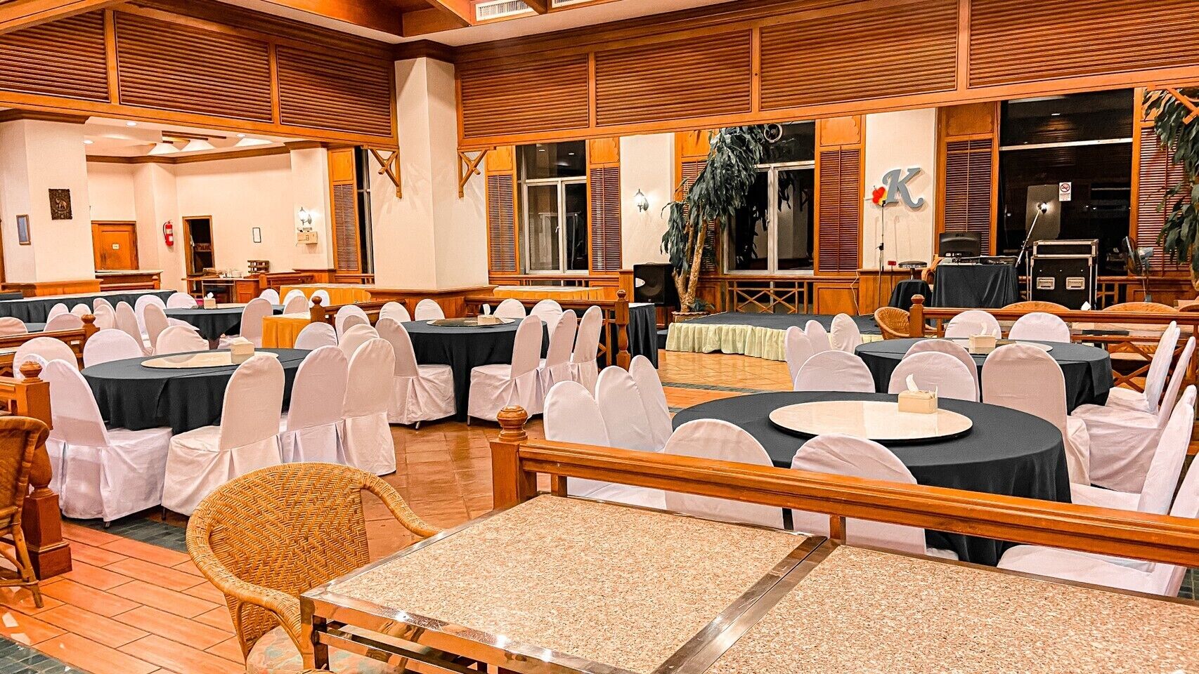 Een feestzaal met ronde tafels en witte stoelen, houten lambrisering en een podium.