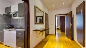 Una cocina moderna con electrodomésticos integrados, piso de madera y un pasillo que conduce a un dormitorio.