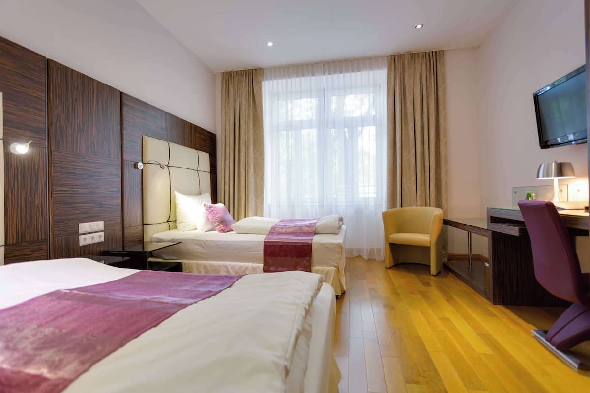 A hotel room with two beds, a desk, a chair, and a TV.