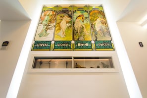 A stained glass window with four panels depicting figures in nature. Below the window, there is a shelf with decorative items. - Best Western Plus Hotel Arcadia (Vienna)