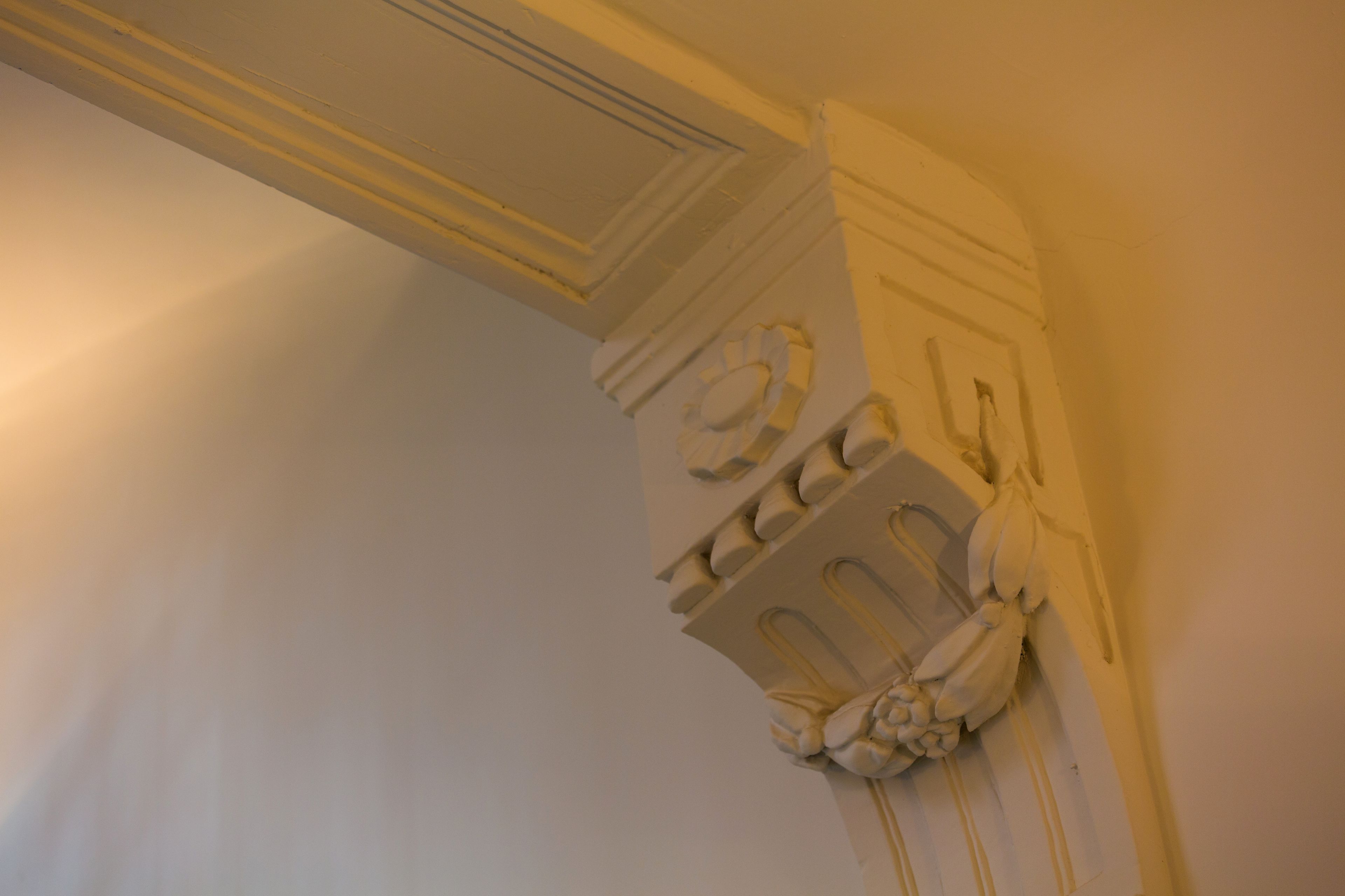 A corner of a room with a white wall and a decorative molding.