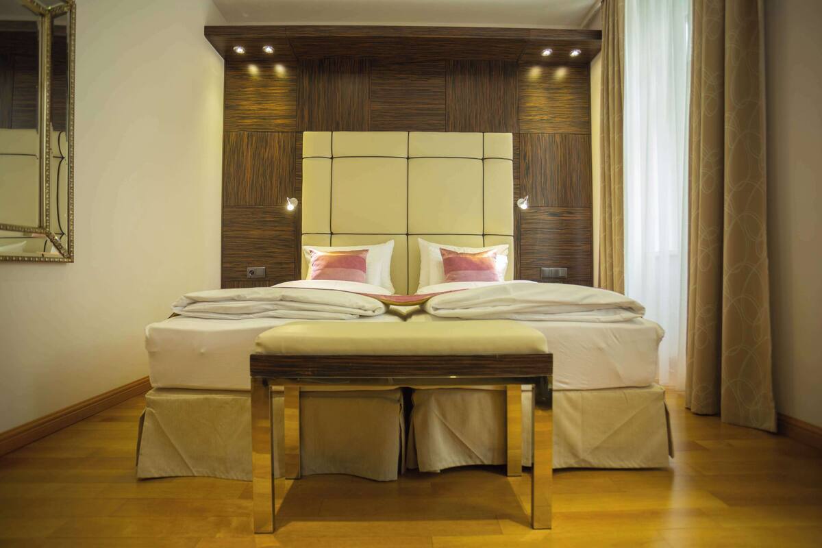 A neatly made bed with a headboard, a bedside table, and a bench in a hotel room.