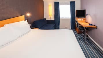 A hotel room with a bed, a desk with a computer, a TV, and a lamp.