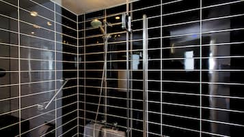 Une salle de bain moderne avec des murs recouverts de carreaux noirs, une douche en verre et un porte-serviettes apparent.