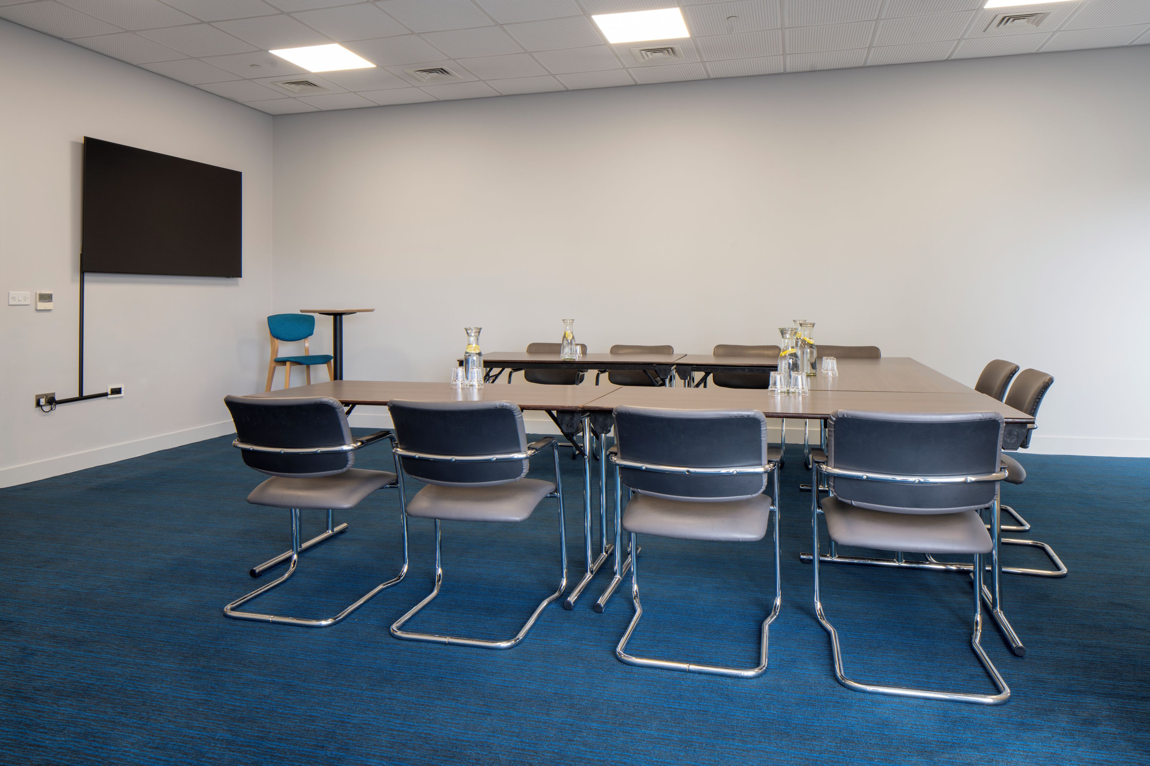 A conference room with a long table, six chairs, and a projector screen on the wall.