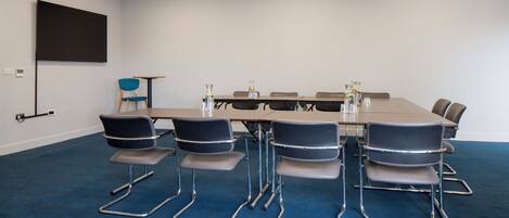 A conference room with a long table, six chairs, and a projector screen on the wall.
