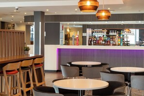 A bar area with a counter, various bottles, and glasses. There are round tables and chairs in the foreground. - Holiday Inn Express Birmingham - Snow Hill by IHG (Birmingham)