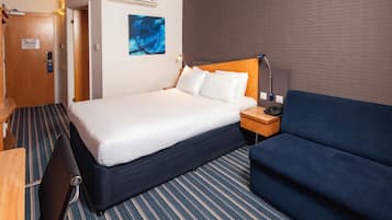 Una habitación de hotel con cama, mesita de noche, lámpara y un sofá azul.