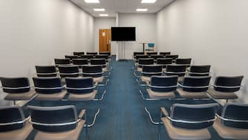 A conference room with rows of chairs facing a black screen, a wooden door, and a small table with a chair.