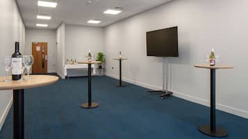 Een vergaderruimte met een groot flatscreen televisietoestel, meerdere tafels met wijnflessen en glazen, en een vloerbedekking.