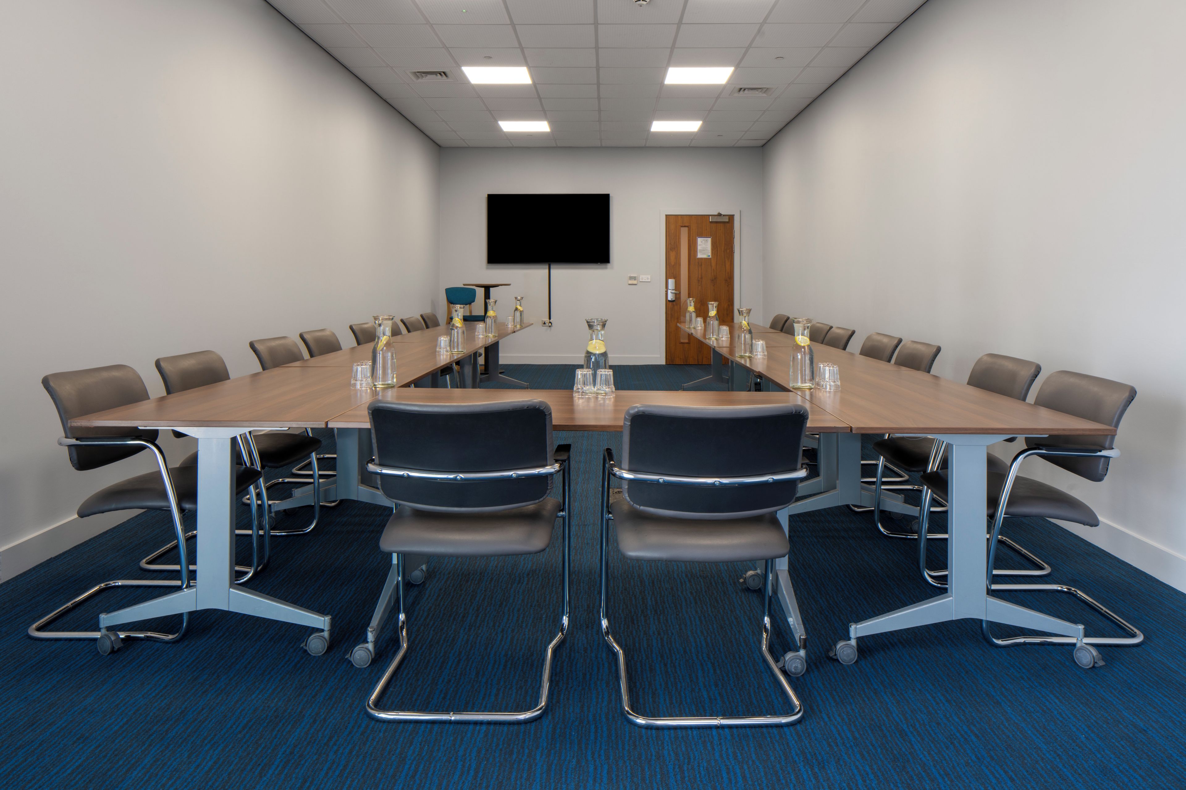 A conference room with a long table, chairs, and a screen on the wall.