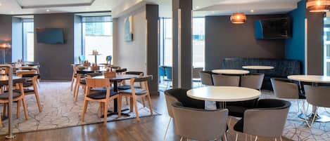 Un comedor moderno con mesas y sillas de madera, suelo estampado y un ventanal con vistas.