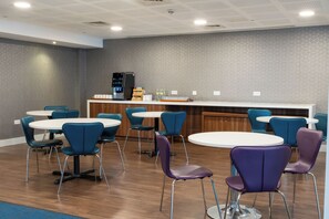 A modern dining area with round tables and chairs, a refrigerator, and a counter with various items. - Holiday Inn Express Birmingham - Snow Hill by IHG (Birmingham)
