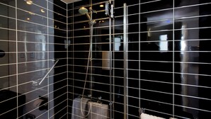 Ein modernes Badezimmer mit schwarzen Fliesenwänden, einer Duschkabine aus Glas und einem sichtbaren Handtuchhalter.