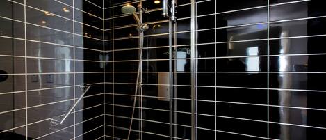 A modern bathroom with black tiled walls, a glass shower enclosure, and a visible towel rack.