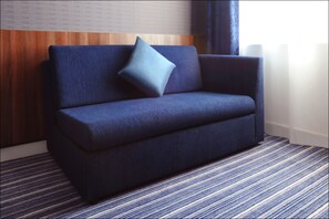 A dark blue sofa with a single light blue pillow against a wooden panel wall and a striped carpet. - Holiday Inn Express Birmingham - Snow Hill by IHG (Birmingham)