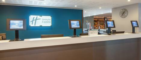 A hotel reception desk with a blue wall, a clock, and three monitors.