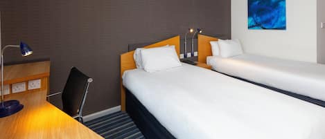 A hotel room with two beds, a desk with a lamp, and an air conditioning unit on the wall.