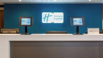 A Holiday Inn Express reception desk with two monitors, a blue wall, and a white counter.