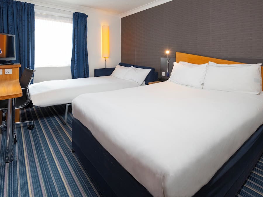 Een hotelkamer met twee bedden, een bureau, een televisie en een lamp.