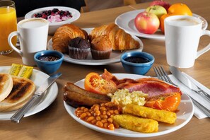 A breakfast table with plates of food, including eggs, bacon, beans, sausages, toast, and pastries. There are also cups of coffee and juice. - Holiday Inn Express Birmingham - Snow Hill by IHG (Birmingham)