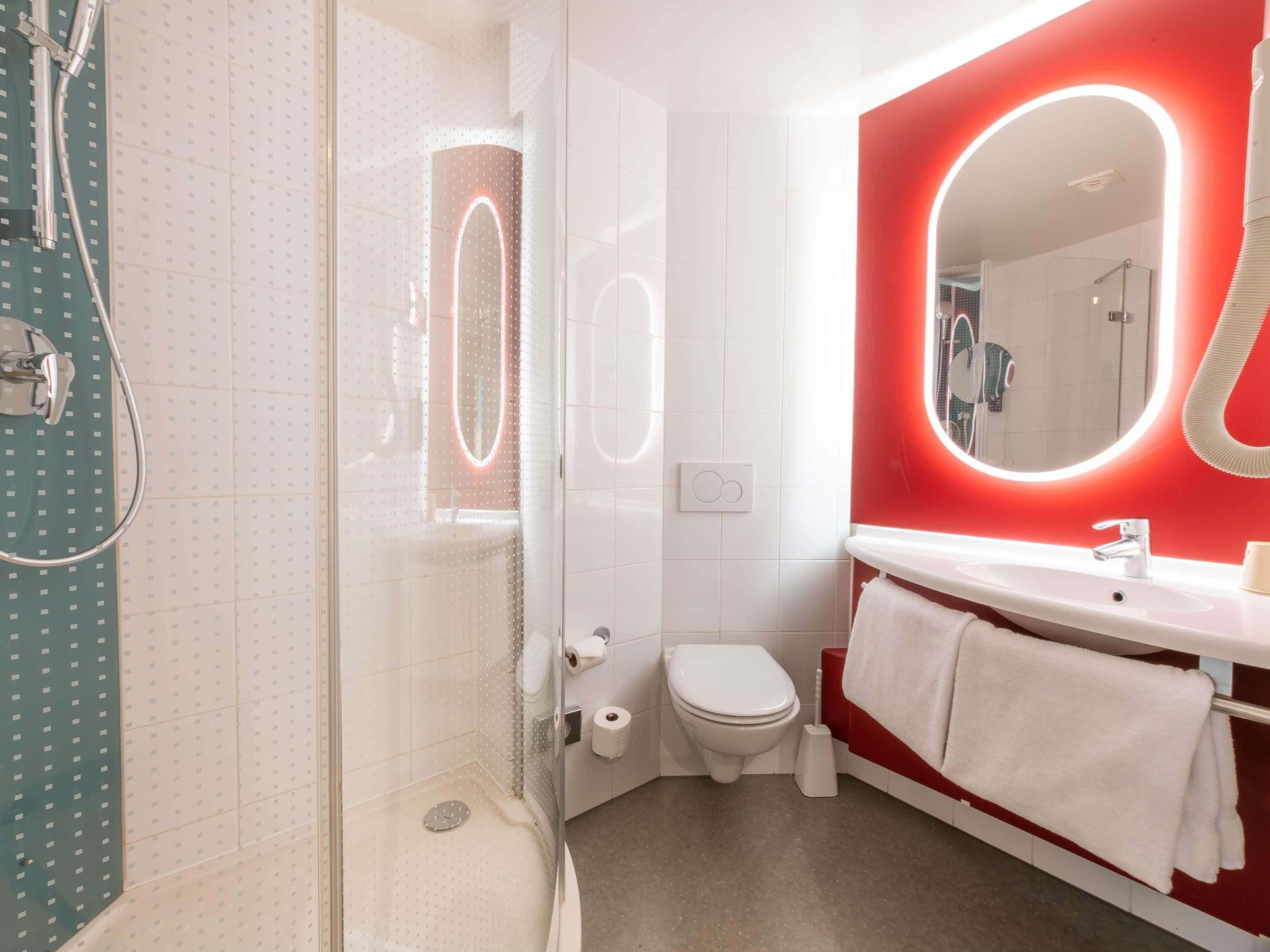 A modern bathroom with a glass-enclosed shower, a white toilet, a red vanity with a mirror, and a white sink.