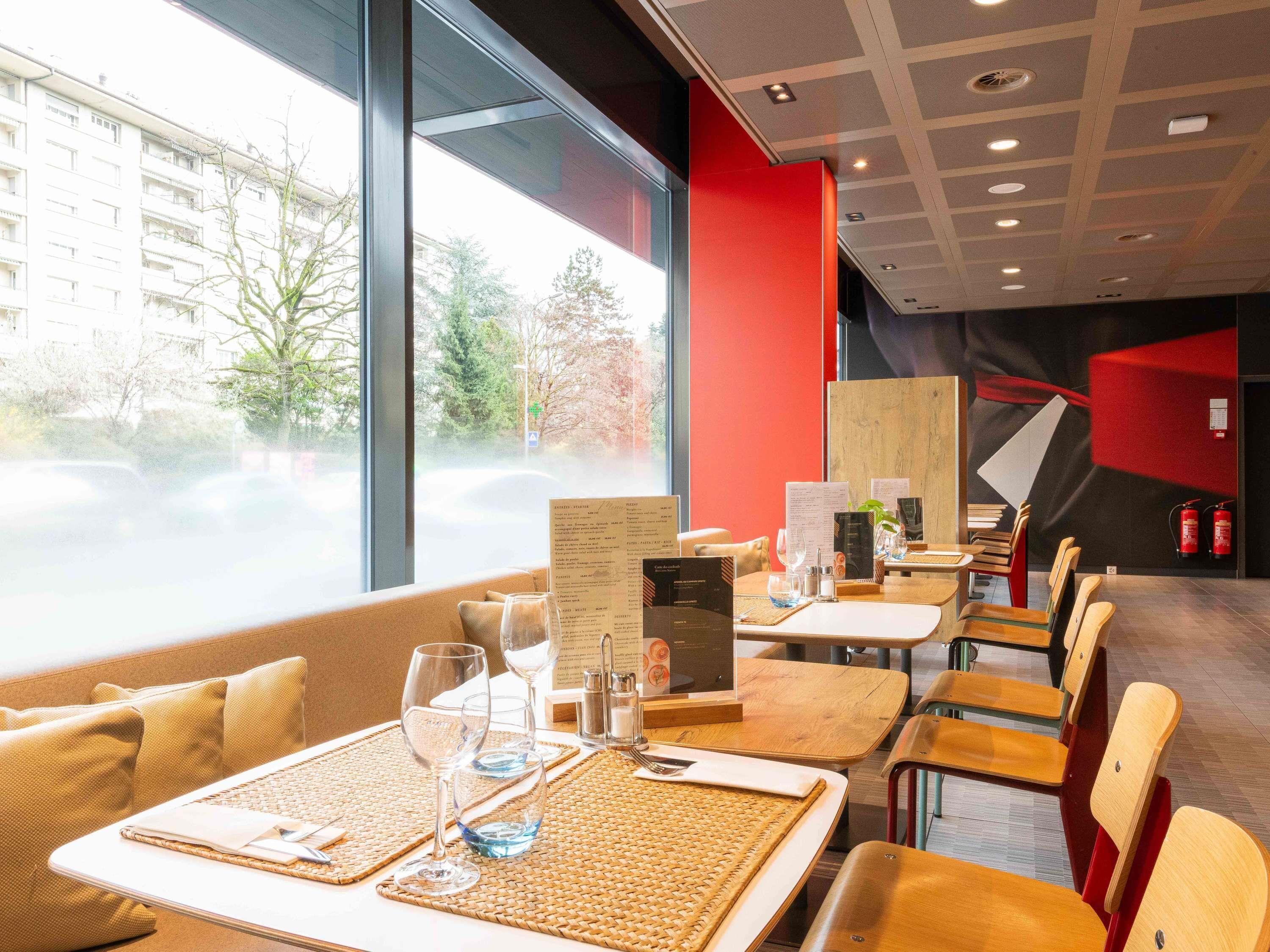 A restaurant with tables set for dining, a menu stand, and a view of the street outside.