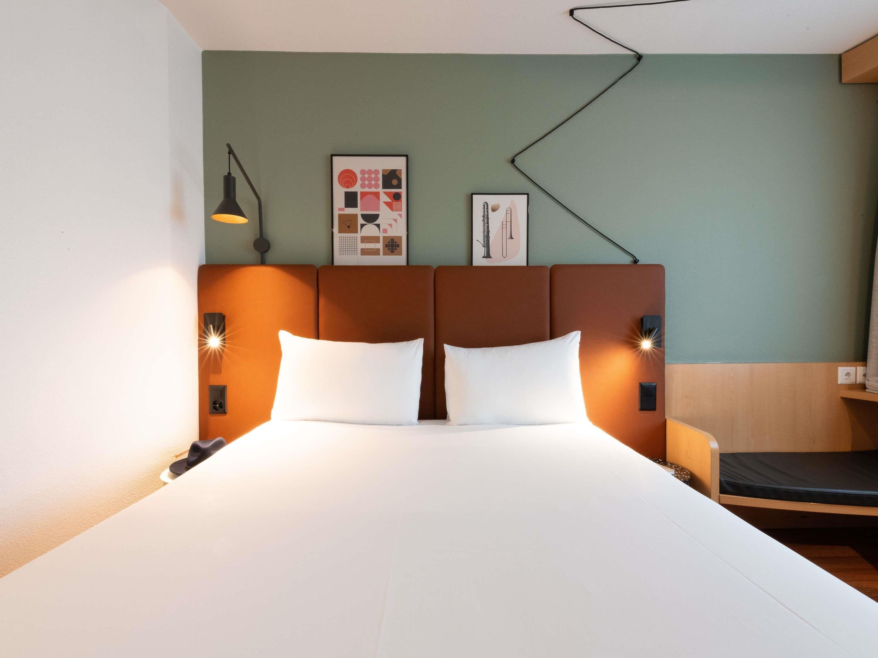 Une chambre d’hôtel avec un lit, deux lampes de chevet, une tête de lit et deux tableaux encadrés accrochés au mur.