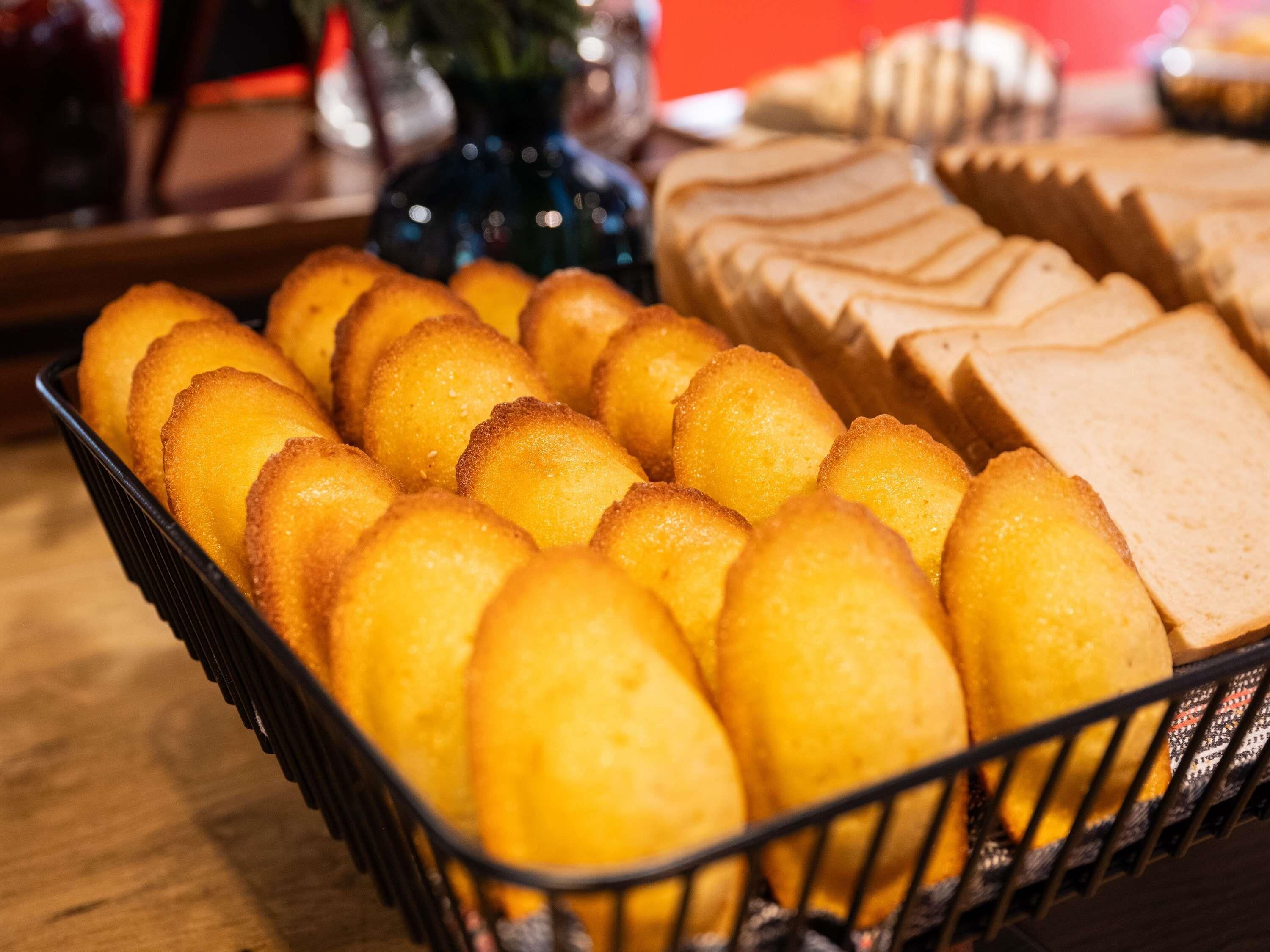 Een schaal met goudbruine gebakjes en een grote rechthoekige taart op een houten tafel.