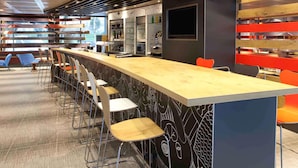 A modern bar area with a long counter, bar stools, and a bar refrigerator. - ibis Geneve Centre Nations (Geneva)