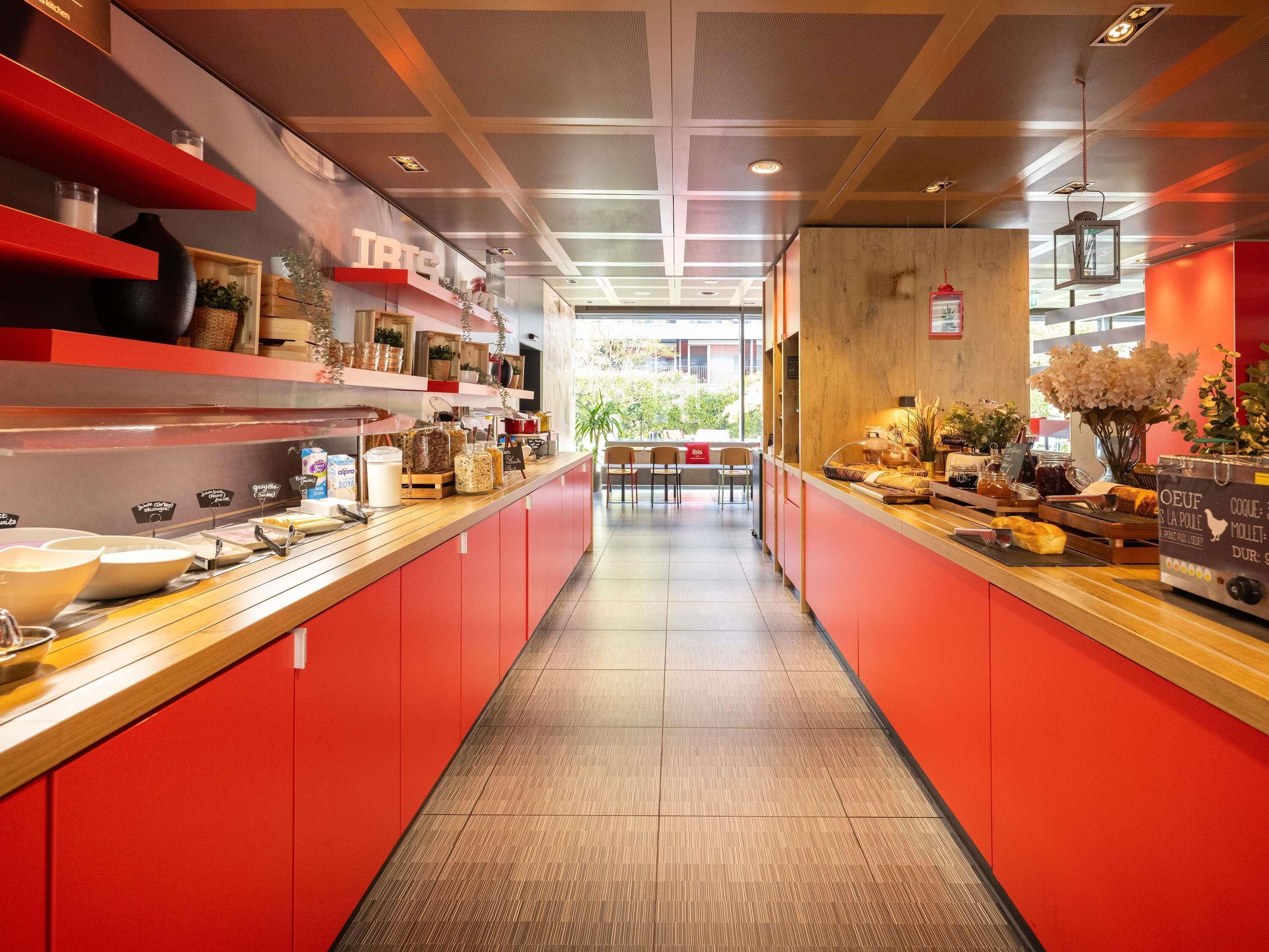 Una cocina moderna con armarios rojos, una encimera amplia con diversos alimentos y vistas al exterior.