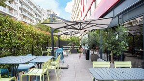 An outdoor patio with tables and chairs, surrounded by greenery and buildings. - ibis Geneve Centre Nations (Geneva)