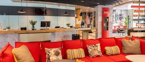 A modern hotel lobby with a red sofa, a laptop on a table, and a reception desk.