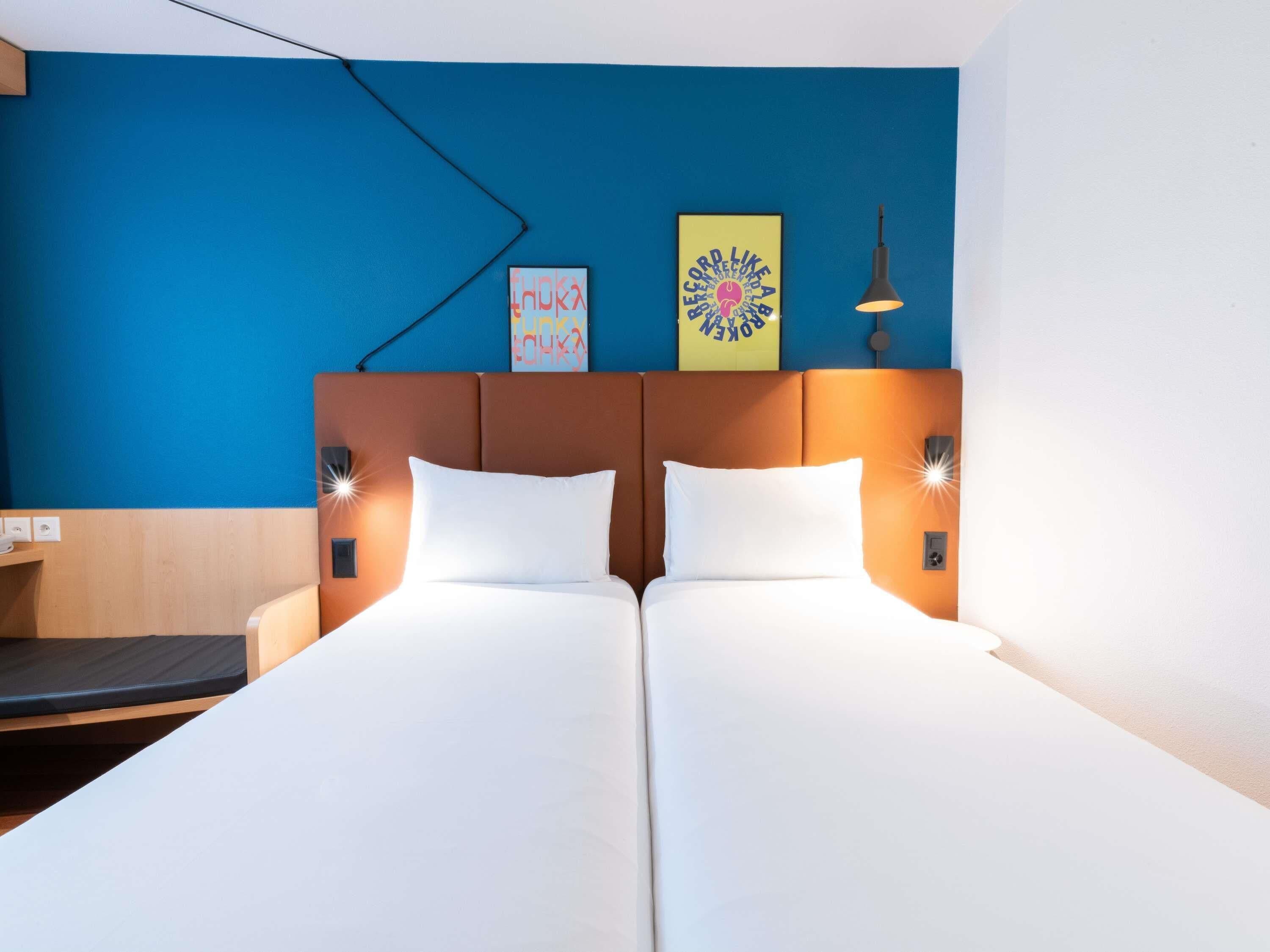 A double bed with white linens, a brown headboard, and two wall-mounted lamps.