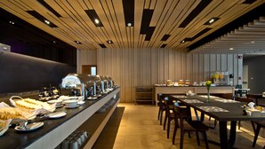 Un espace moderne dédié au petit-déjeuner, avec un buffet, une table à manger entourée de chaises et une cuisine en arrière-plan.