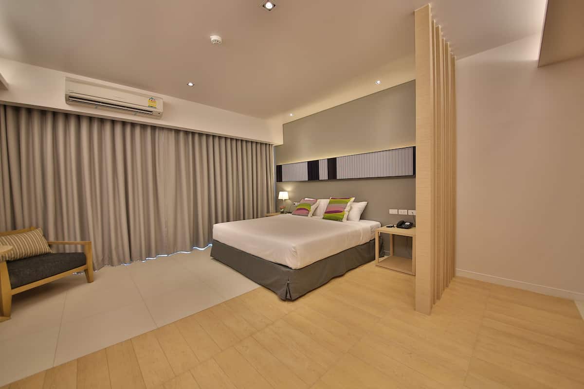A modern hotel room with a large bed, a bedside table, a desk, and an air conditioning unit.