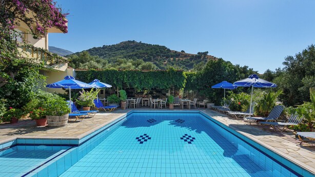 Une piscine dont le fond est décoré de motifs en mosaïque, entourée de chaises longues et de parasols, avec en arrière-plan une vue sur une colline.