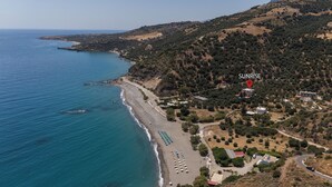 Vue aérienne d’une zone côtière avec une plage, un point précis indiqué et portant le nom « SUNRISE », et un paysage vallonné environnant.