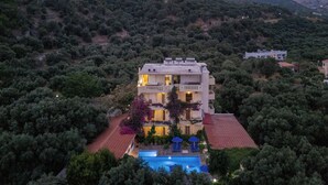 Un immeuble à plusieurs étages doté d’une piscine, entouré d’une végétation luxuriante et de collines.